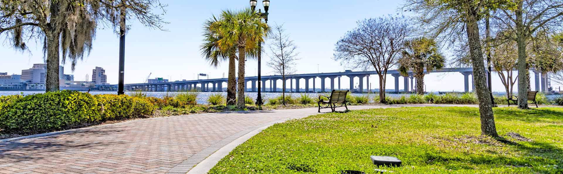 brick walking path next to wiver and bridge on a sunny day