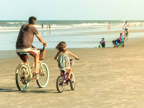 Father and daughter riding bicycles on beach